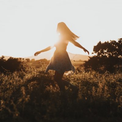Woman dancing in a grassy field at sunset.